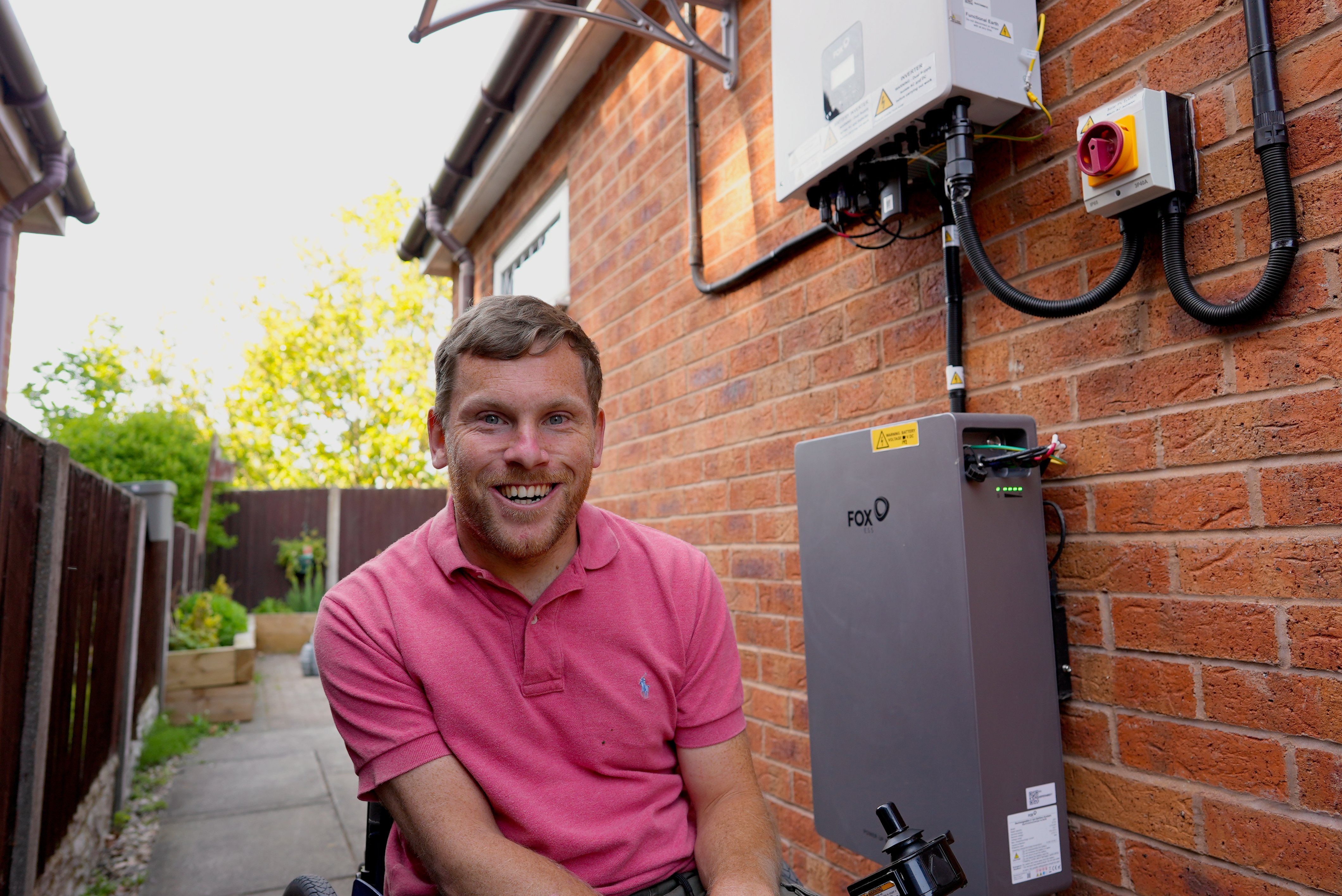 Man sat outside his house with a heat pump on the exterior of his house