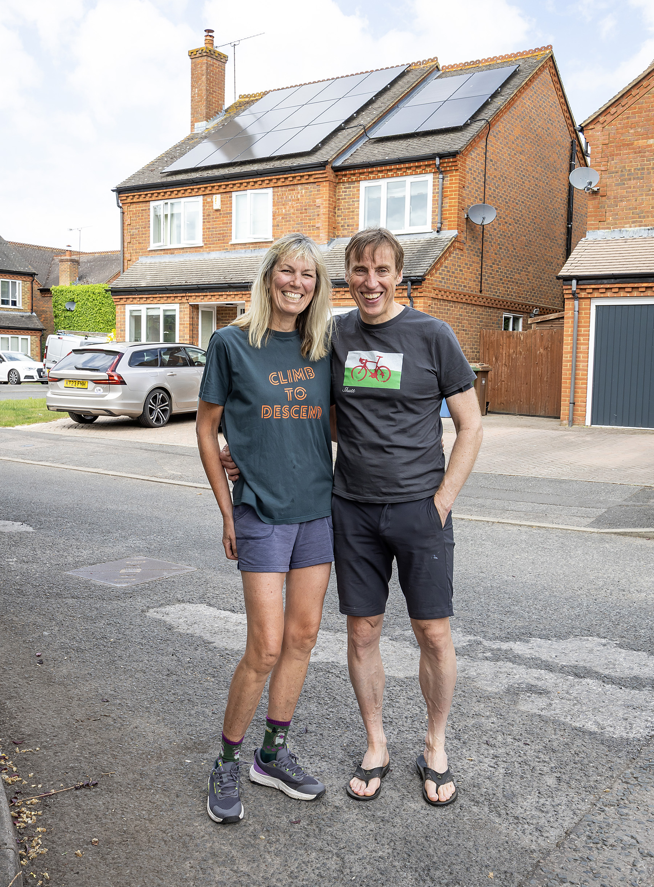 Happy couple stood outside their house showing their solar panels on the roof